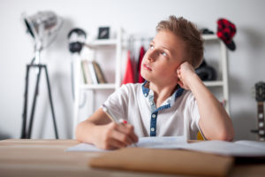 Distracted preteen boy trying to doing homework and thinking about something