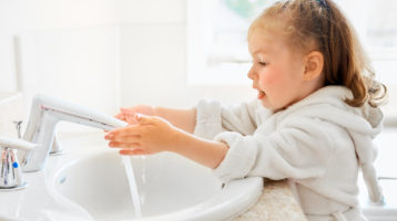 Cute little girl is washing hands under running water.